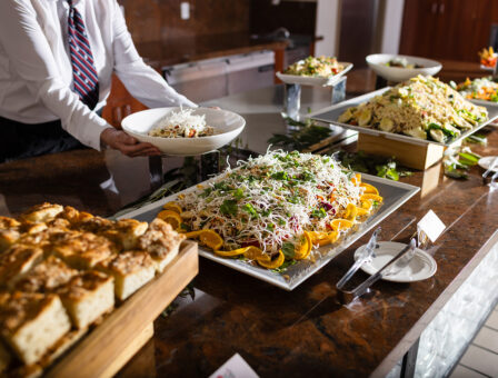 A service plates food from a lunch buffet displaying various platters of salads and appetizers.