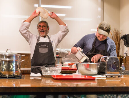 Man flips pizza dough in a playful Chef Events demonstration.