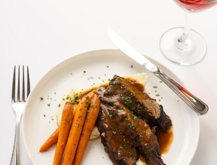A steak and roasted carrot dinner with a glass of wine.