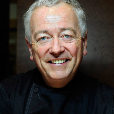Man with graying hair and black chef's coat smiles at the camera.