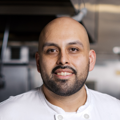 Man with dark mustache and beard wearing white chef's coat