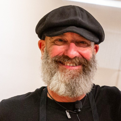 community-class-dave-the-butcher-sq Man with graying beard wears a black-brimmed cap and black T-shirt while smiling at the camera.