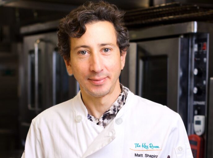 Man in white chef coat stands in kitchen