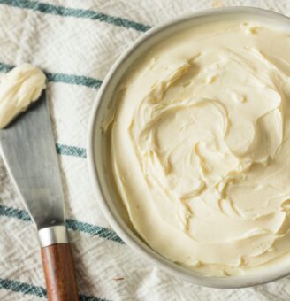 Small bowl of fresh soft cheese on a white and green striped dishtowel with knife set beside it with scoop of cheese