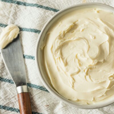 Small bowl of fresh soft cheese on a white and green striped dishtowel with knife set beside it with scoop of cheese