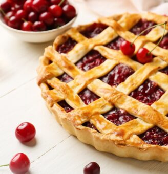 Cherry pie with lattice crust and cherries in a nearby bowl