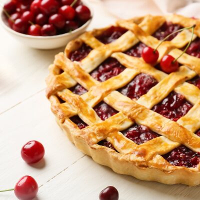 Cherry pie with lattice crust and cherries in a nearby bowl