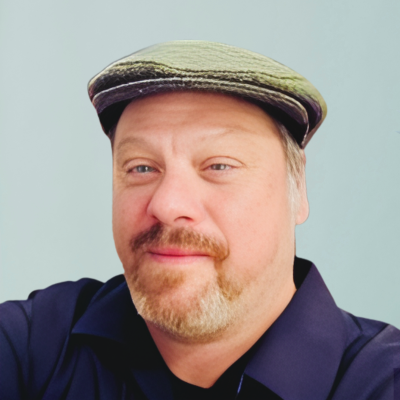 Man with light brown beard and gray cap smiles at the camera