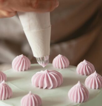 Person using piping bag to create pink swirls on white cake top