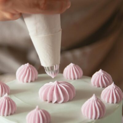 Person using piping bag to create pink swirls on white cake top