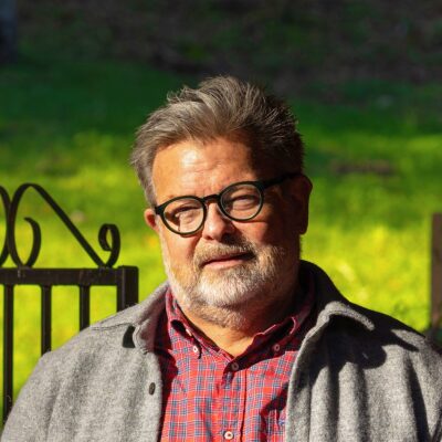 Man with graying hair and glasses wearing plaid shirt and sweater