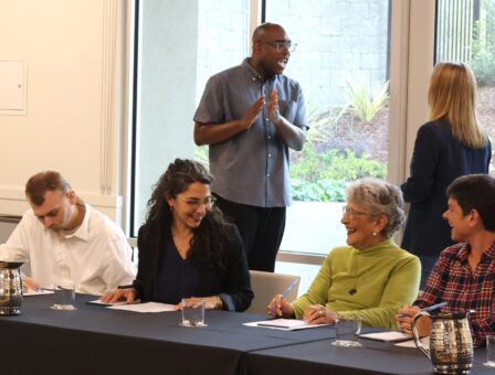 People chat at table and behind them two others stand talking by window