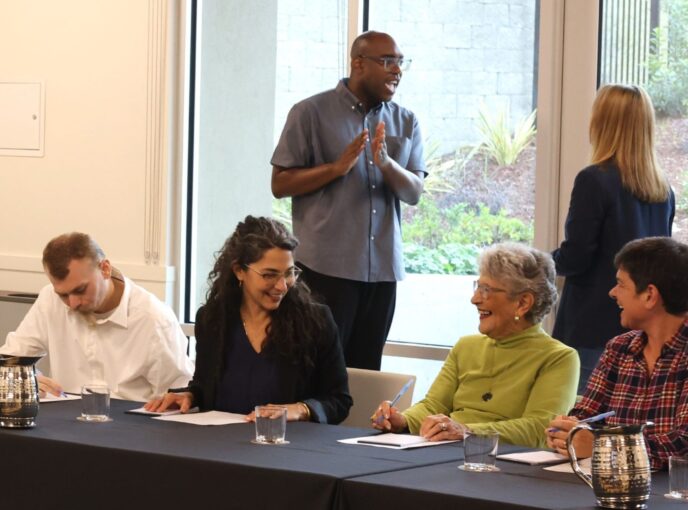 People chat at table and behind them two others stand talking by window