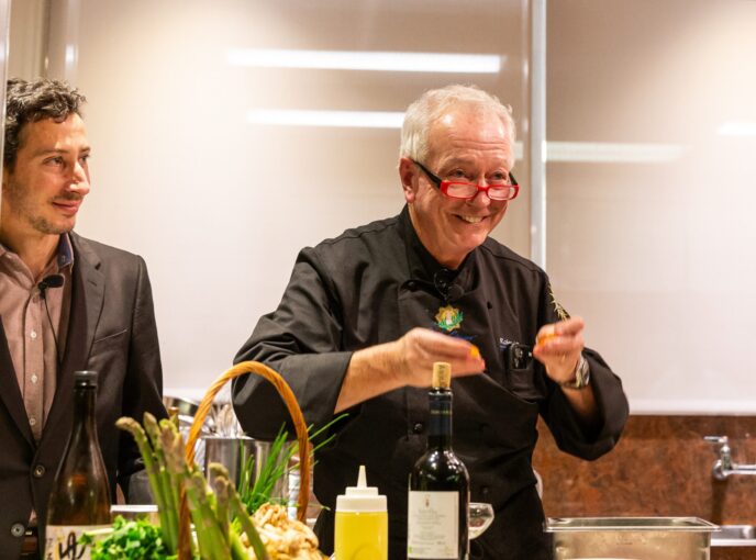 chef with black coat and glasses gestures while holding two lemons