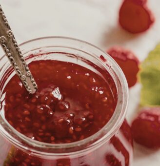 Jar of fresh raspberry jam with silver spoon in it