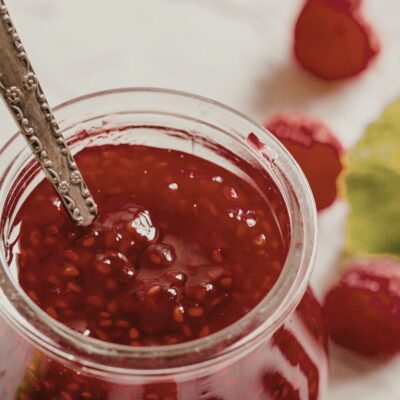 Jar of fresh raspberry jam with silver spoon in it