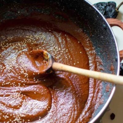 Bowl of mole sauce sprinkled with sesame seeds and a wooden spoon in it