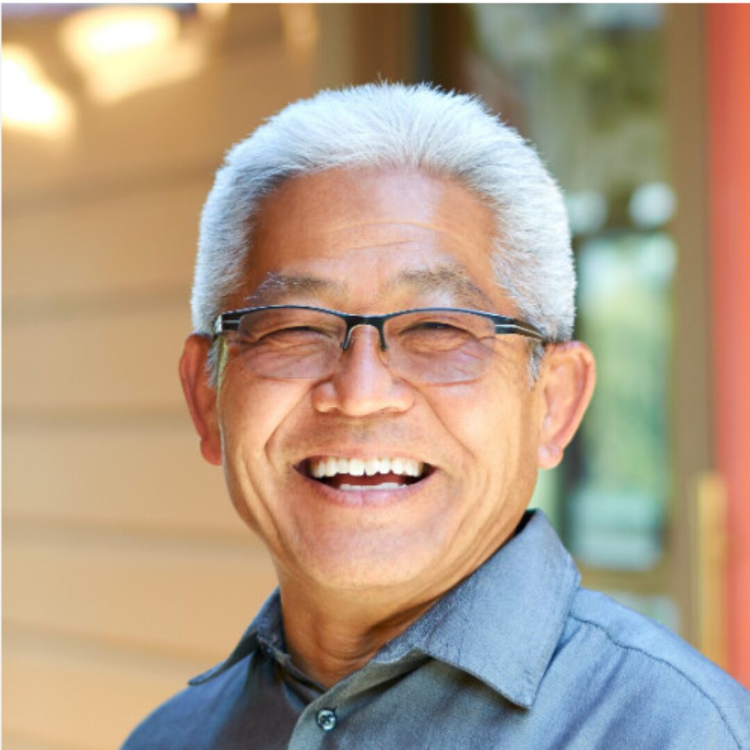 Man with short white hair abd glasses smiles at camera