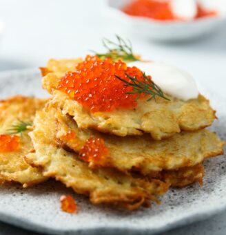 Golden latkes on a plate topped by caviar and dill