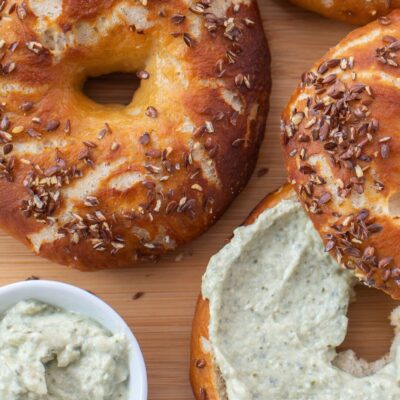 Fresh bagels topped with seeds on board next to schmear of cream cheese and herbs
