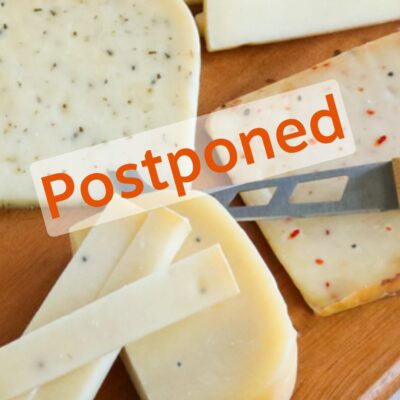 Slices of artisan cheese on a board with word 'postponed' on top