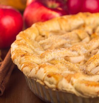 apple pie with lattice top and red apples in th background
