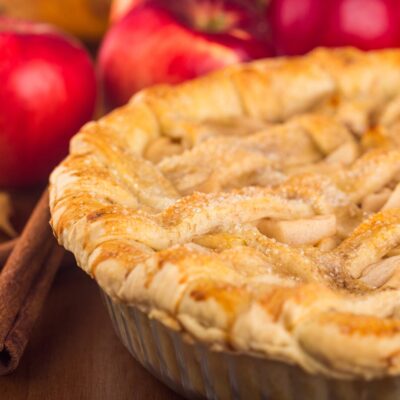 apple pie with lattice top and red apples in th background