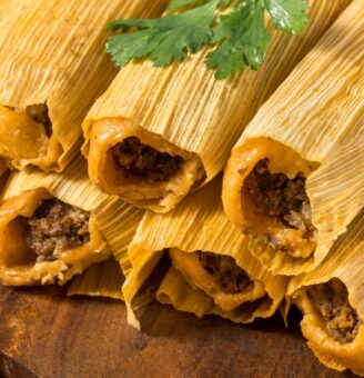 Tamales wrapped in corn husks stacked on a board with cilantro