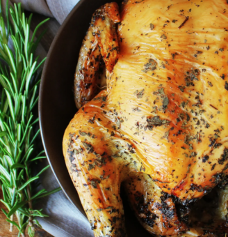 Whole golden roast chicken in a pan with rosemary